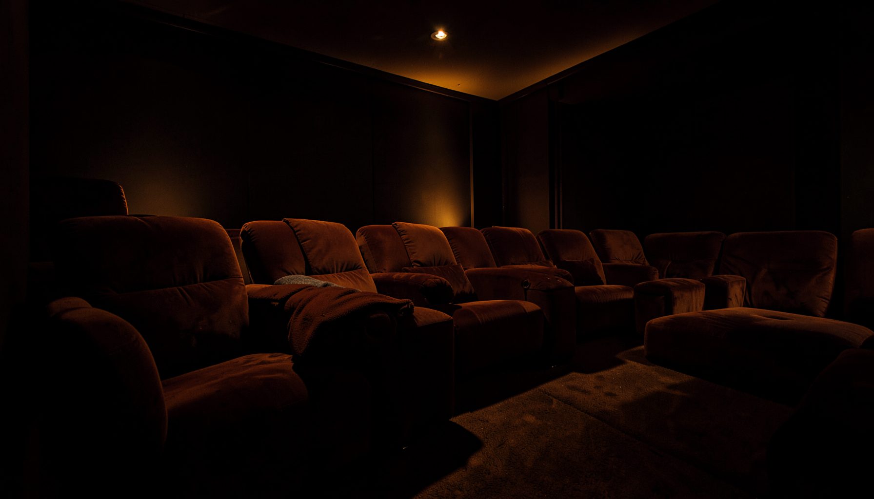 Wide cinematic panorama of a darkened home theater setup with warm amber accent lighting and plush seating, immersive and inviting