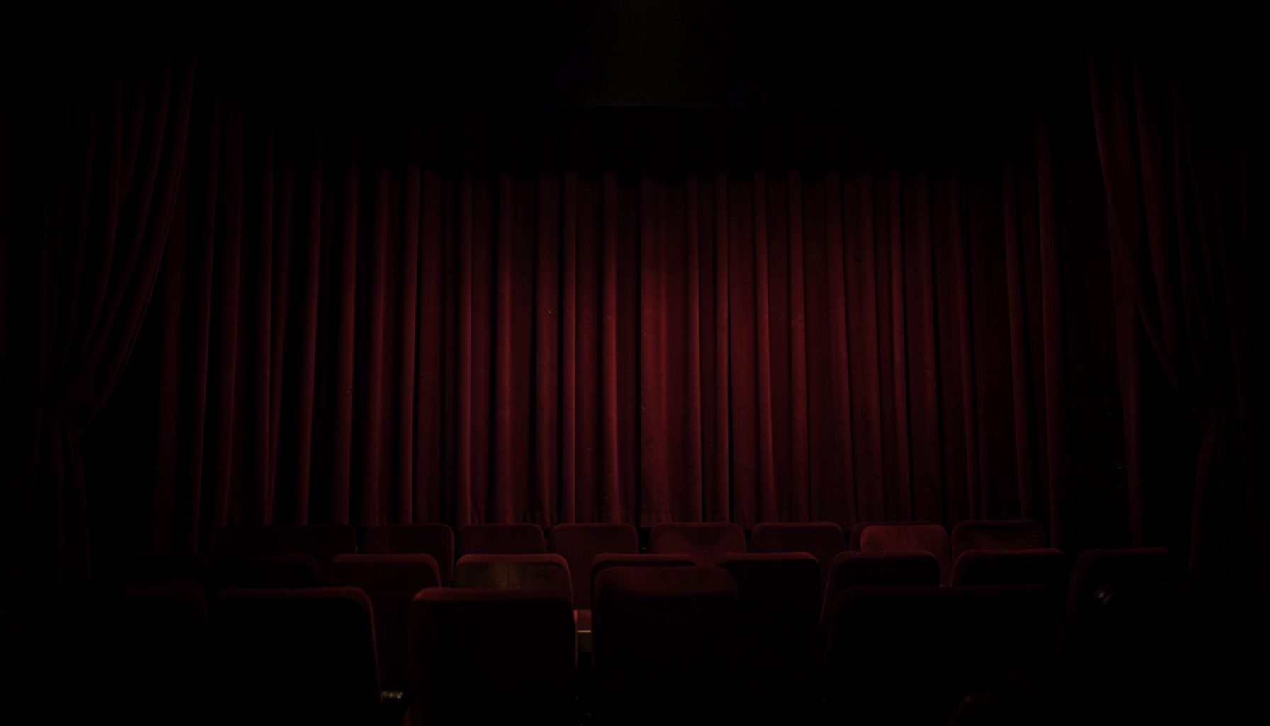 Dark cinematic theater interior with deep red curtain folds and soft ambient glow, moody and dramatic atmosphere