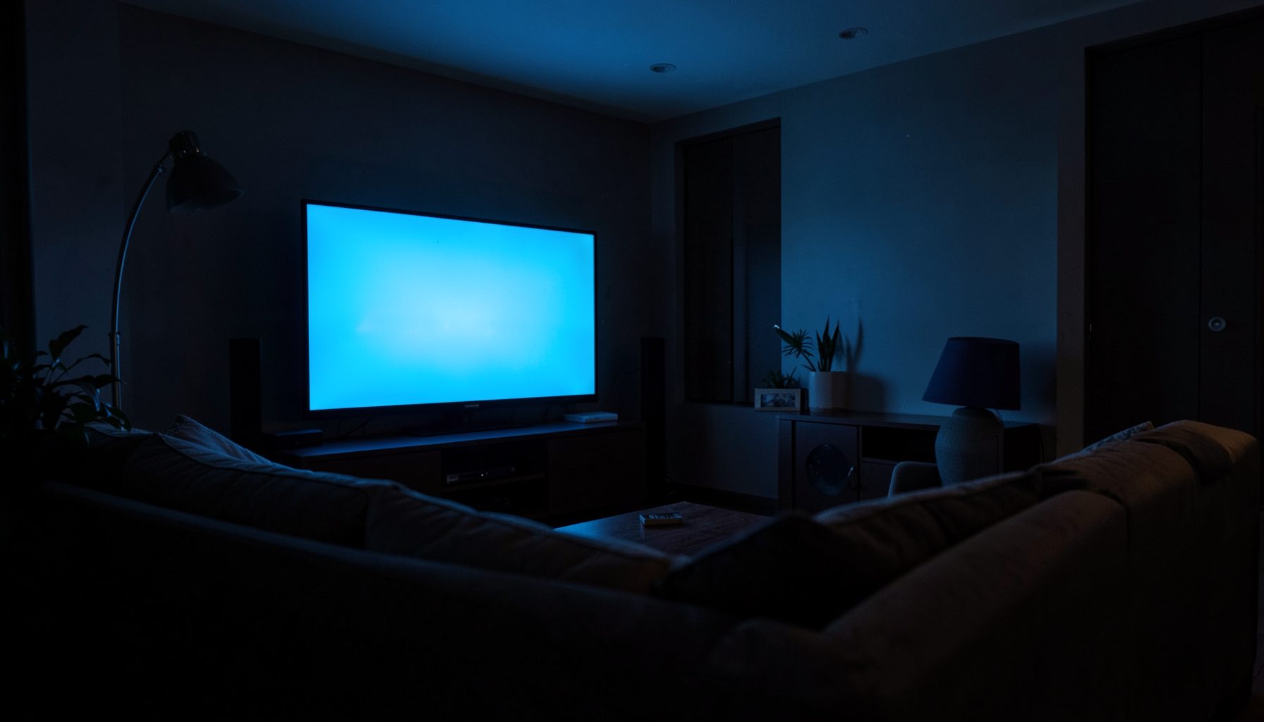Dimly lit living room with a large television screen glowing in cool blue tones, casting soft light across a cozy sofa and dark surroundings